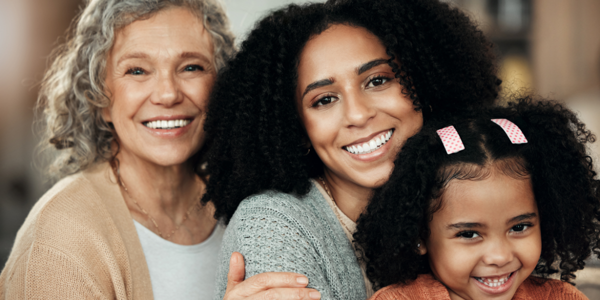 Three people hug each other closely and smile: a grandmother, a mother, and her child daughter
