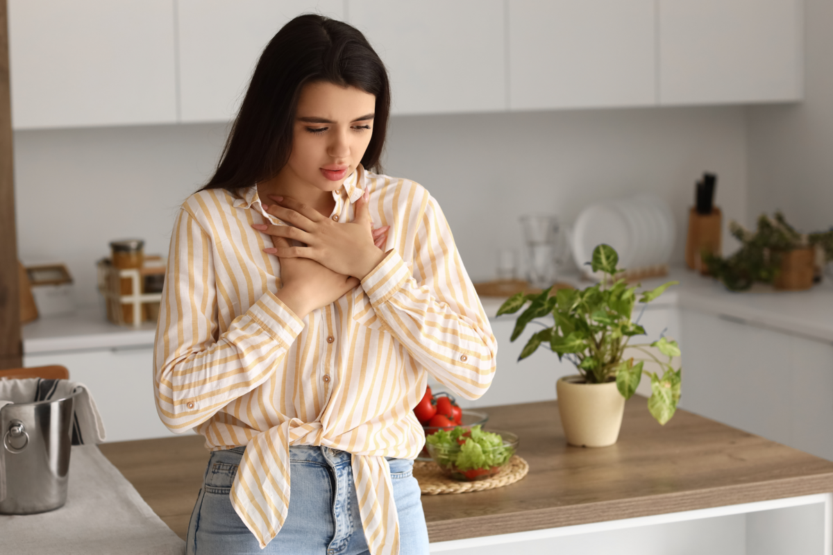 A woman holds her chest with a worried look while standing in a kitchen