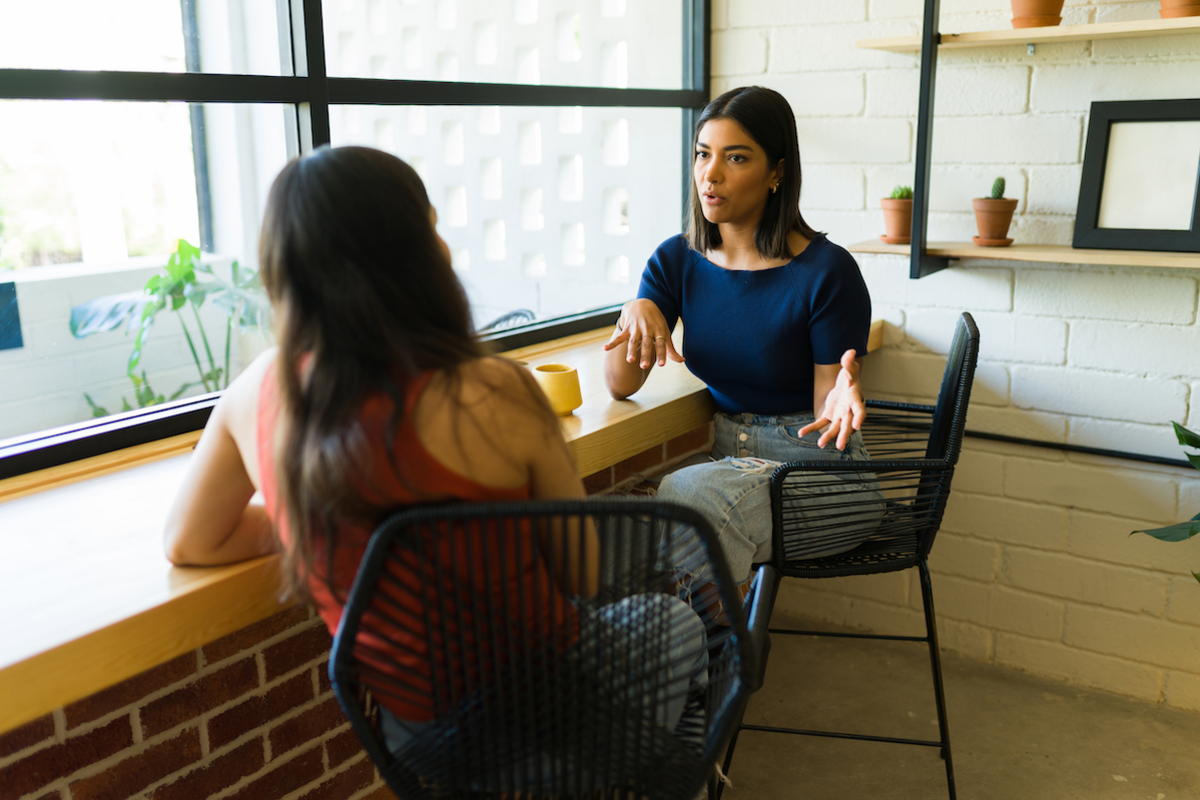 Two people sit at a counter with coffee mugs and hold a conversation