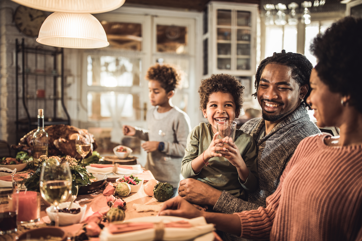A family with two young children smiles while sitting along one side of a large, decorated table set for a holiday meal.