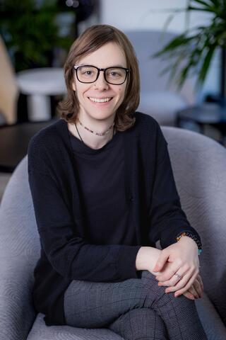 Enea Mastaka sits in an office chair and smiles warmly.