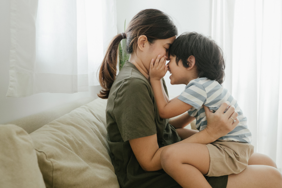 A mother holds her child on her lap and snuggles them face to face