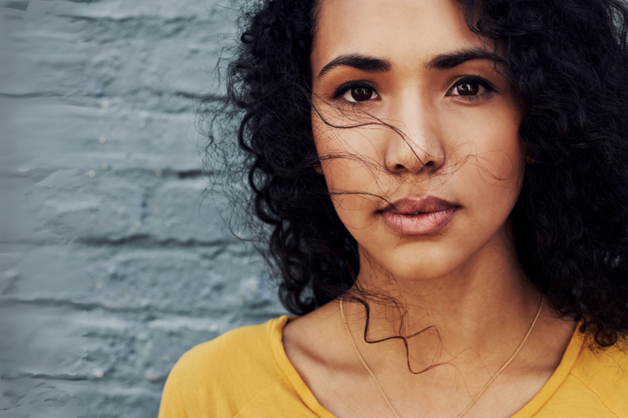 A Latina woman holds a deep stare against a brick wall