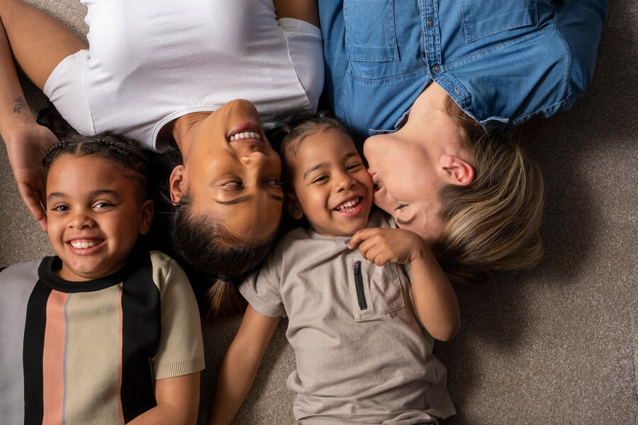 Mixed-race family of two mothers and two children smiling and laying on the floor
