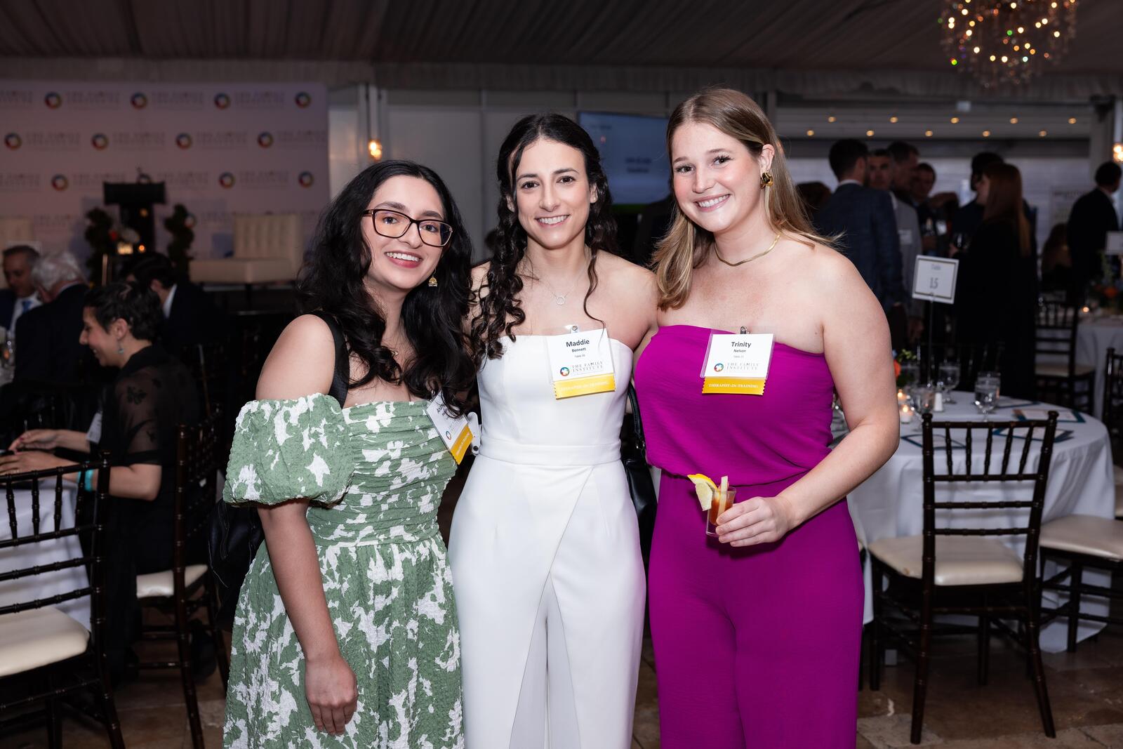 Three graduate students of The Family Institute stand together in the dining room at the Gratitude Gala, smiling.