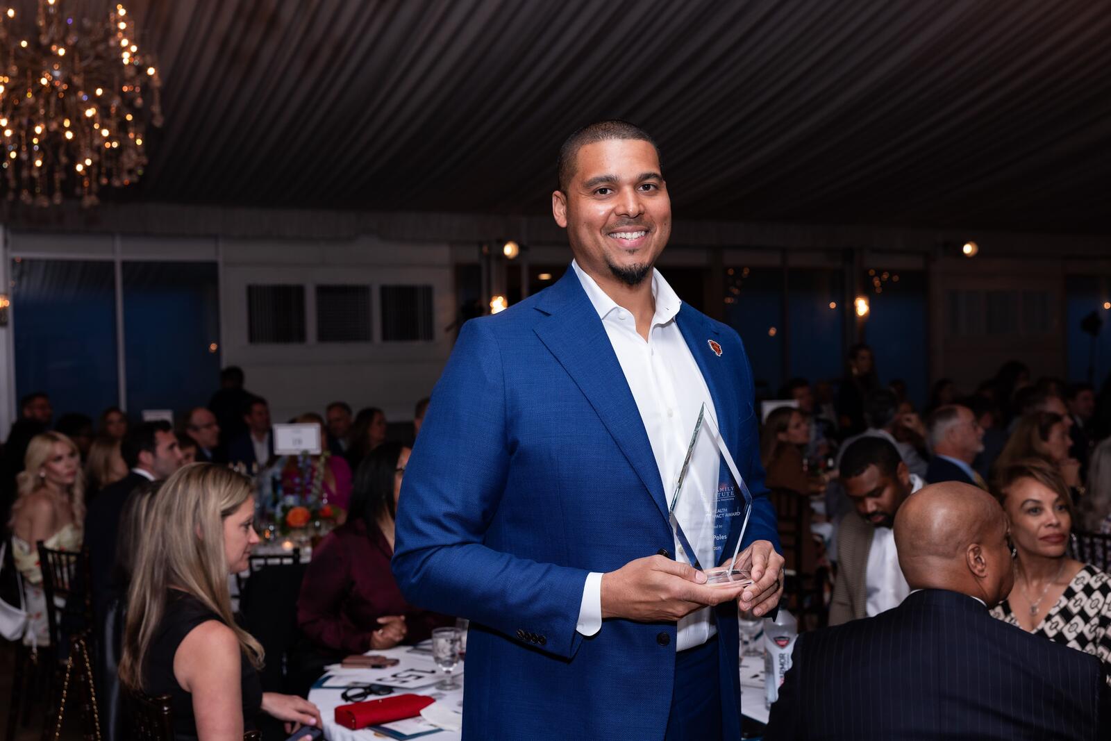 Ryan Poles stands and smiles while holding his award, a diamond crystal plaque.