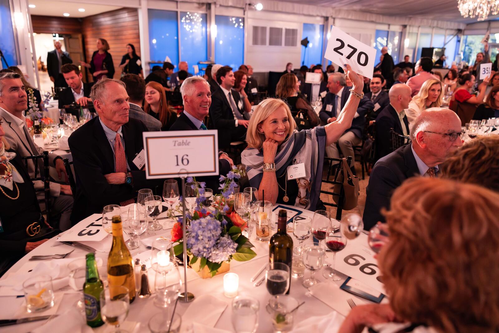 In a crowded room, guests hold up signs with numbers on them in the live auction.