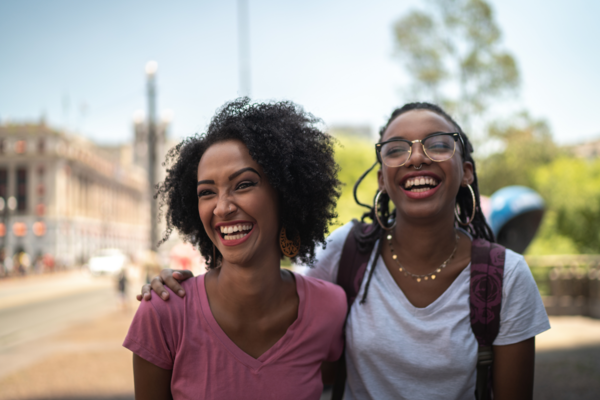 A mother's teenage child, who wears a backpack, puts their arm around her as they both smile and laugh