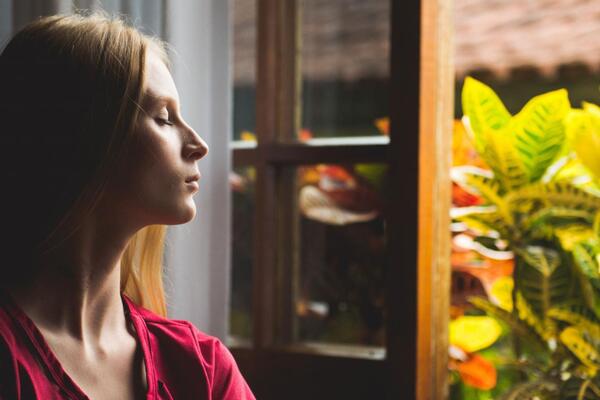 Woman sits by an open window, eyes closed, meditating