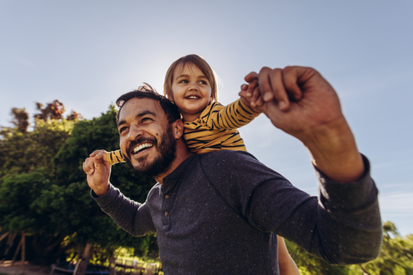 A parent smiles while walking outside with their child on their back