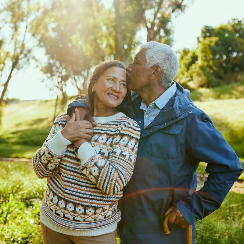 An older couple smile and embrace in the sunshine.